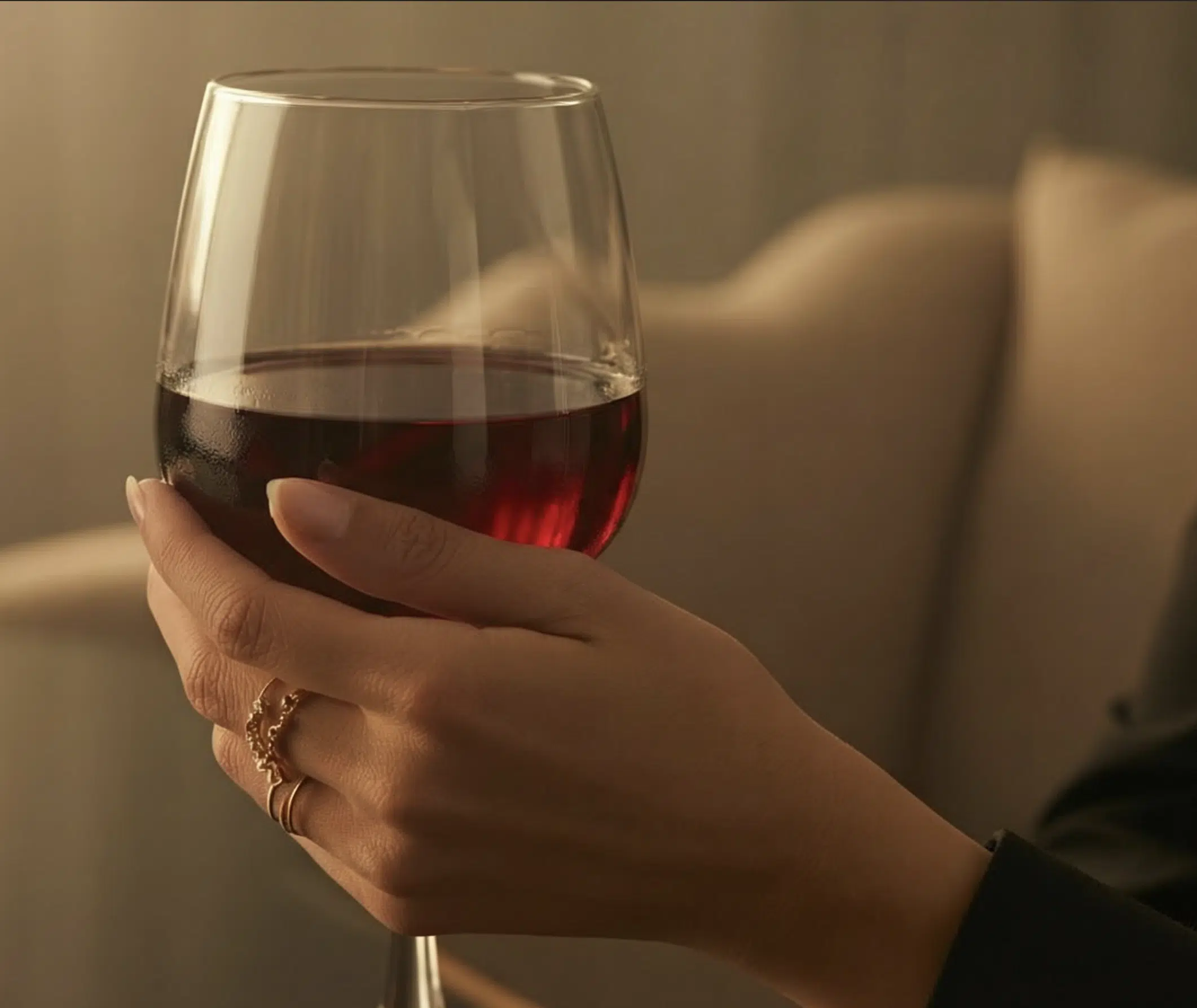 Verre de vin rouge tenu en main dans une lumière chaleureuse, univers Wines and Tees